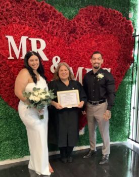 A bride and groom are posing for a picture in front of a large red heart.