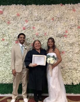 A bride and groom are posing for a picture in front of a flower wall.