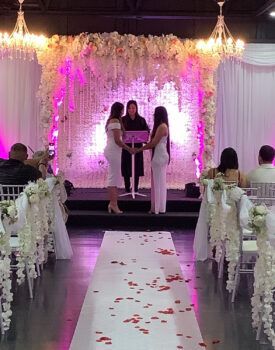 A wedding ceremony is taking place in a room decorated with flowers.