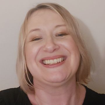 Smiling blonde person in a black shirt against a plain light wall