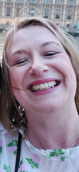 Smiling woman in a floral top, close-up selfie outdoors with a building in the background