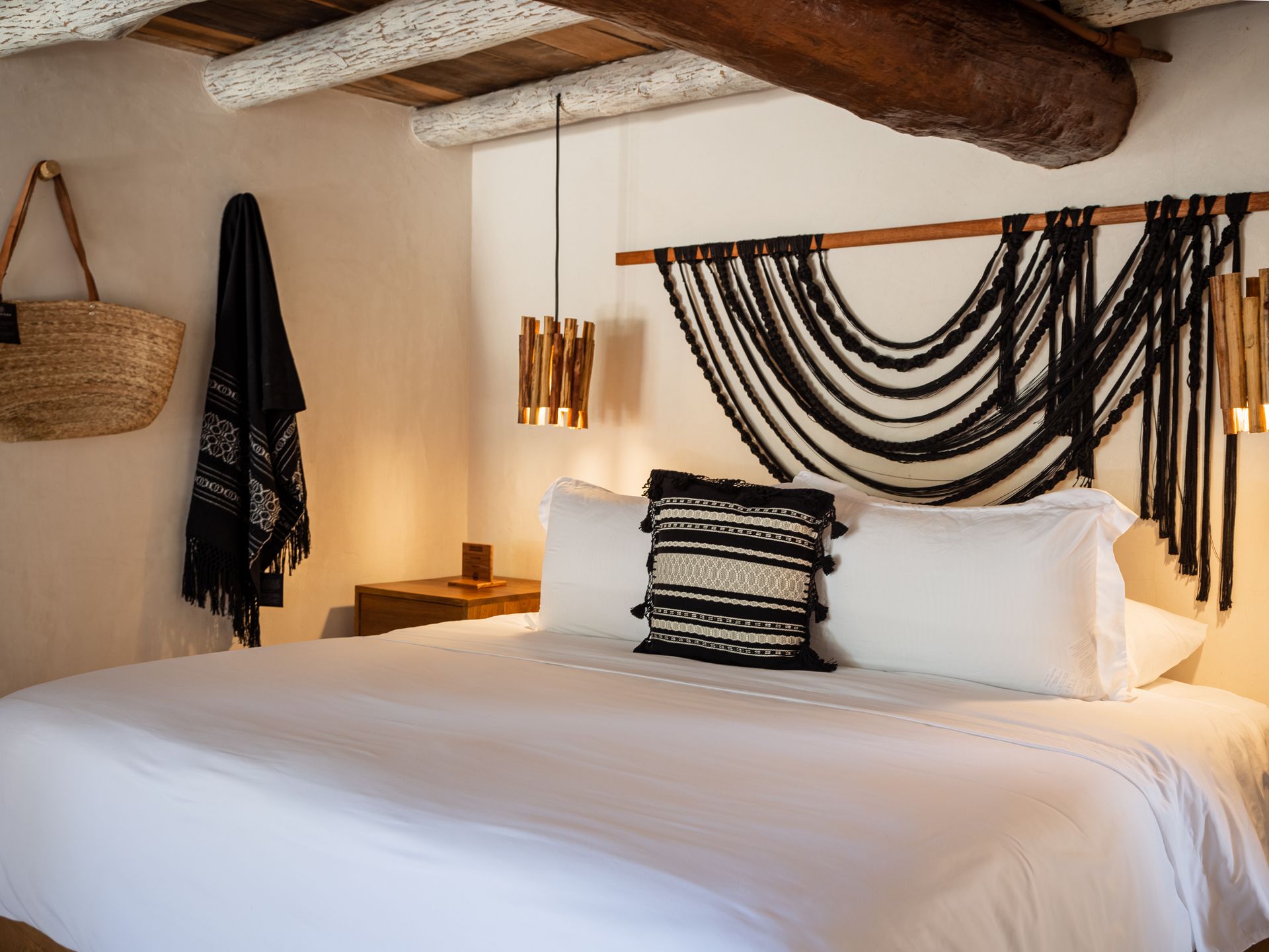 Bedroom with a large white bed, black macrame headboard, woven bag, and hanging lights.