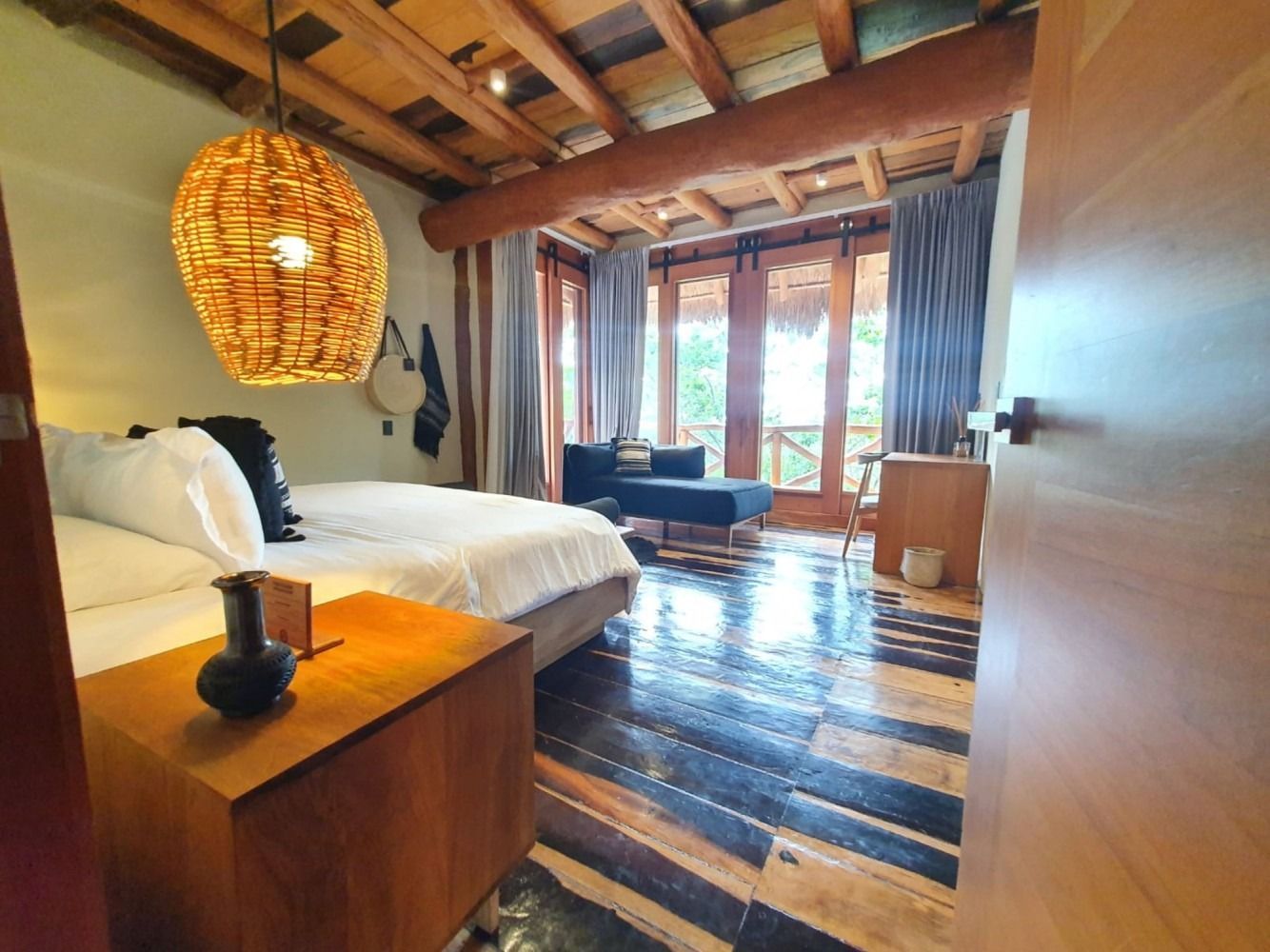 Bedroom with wooden ceiling, floor, and furniture.  A bed, couch, and open door to a balcony are visible.