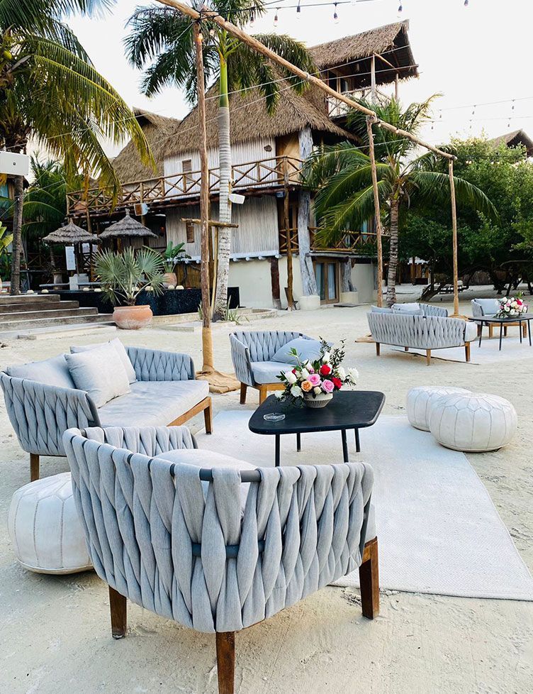 Outdoor lounge area with woven gray chairs, white ottomans, a black coffee table, and flower arrangement.
