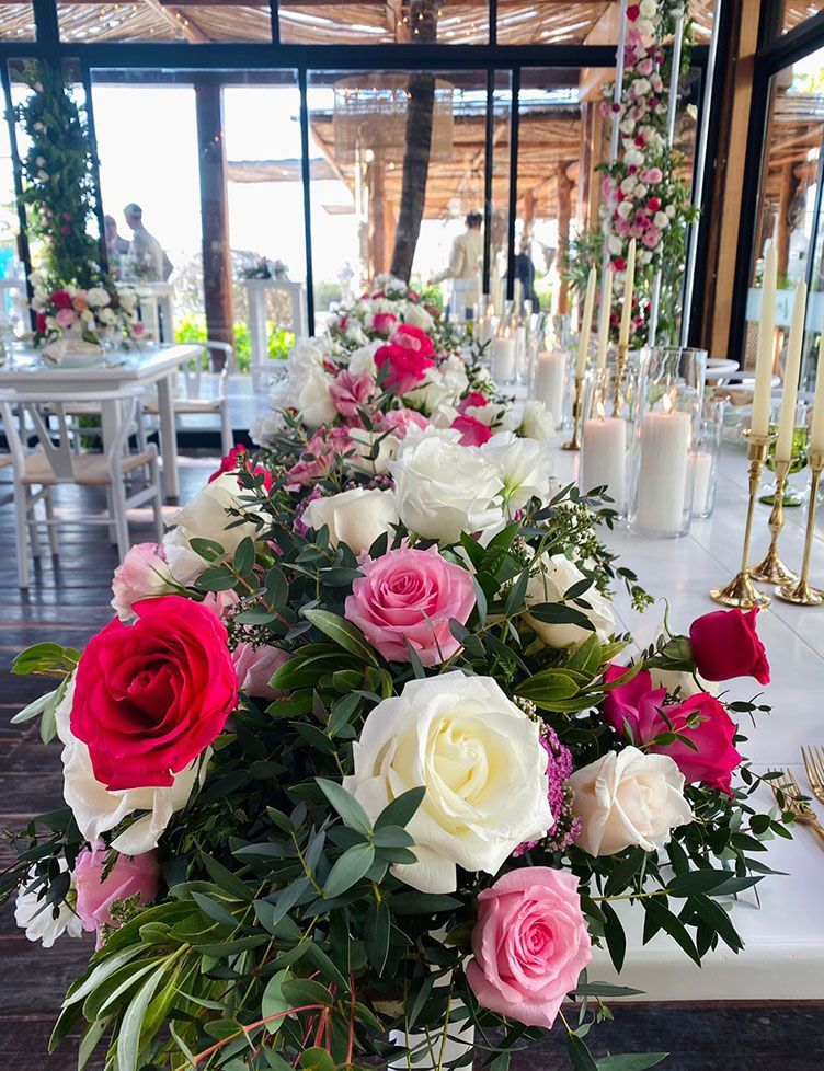 Close-up of a floral centerpiece with pink and white roses on a long table, outdoor setting.