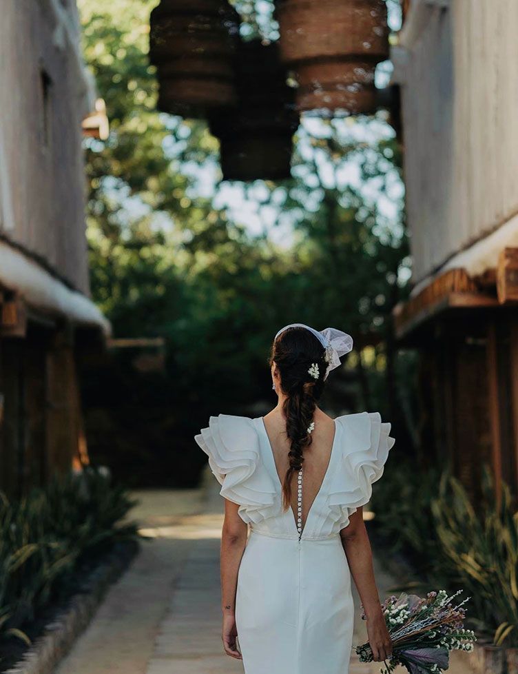 Bride in white dress with ruffled sleeves walks away, holding bouquet, down a pathway.