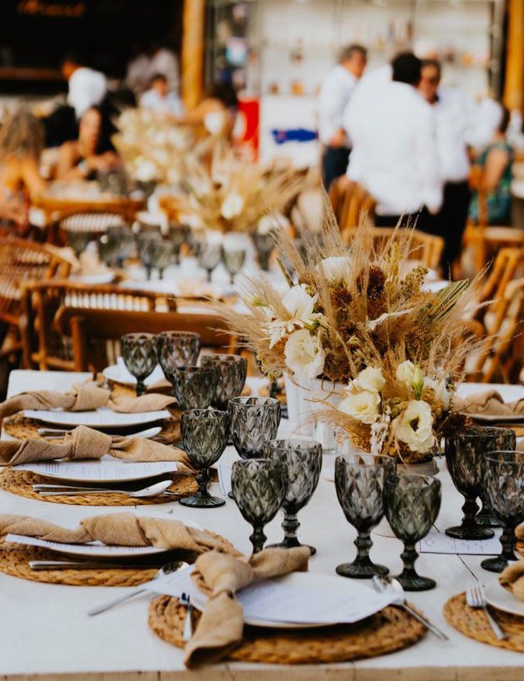 Wedding reception table with floral centerpiece, grey goblets, and beige place settings, outdoor setting.