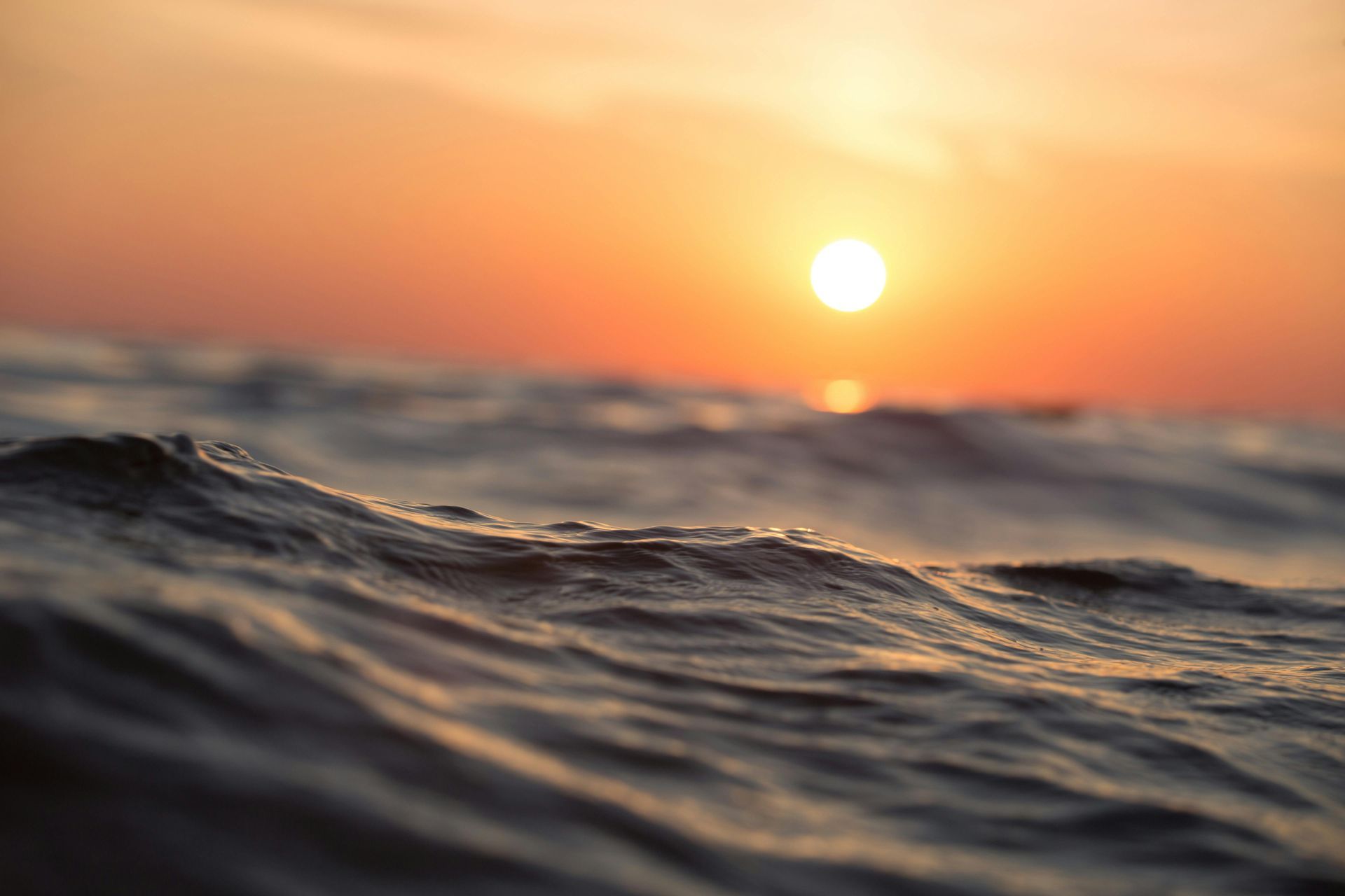 Waves on a dark ocean at sunset with a bright orange sky and sun.