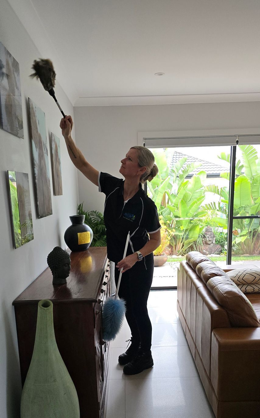 A cleaner is reaching up and dusting frames on a wall — A Place 2 Shine In Bolwarra, NSW