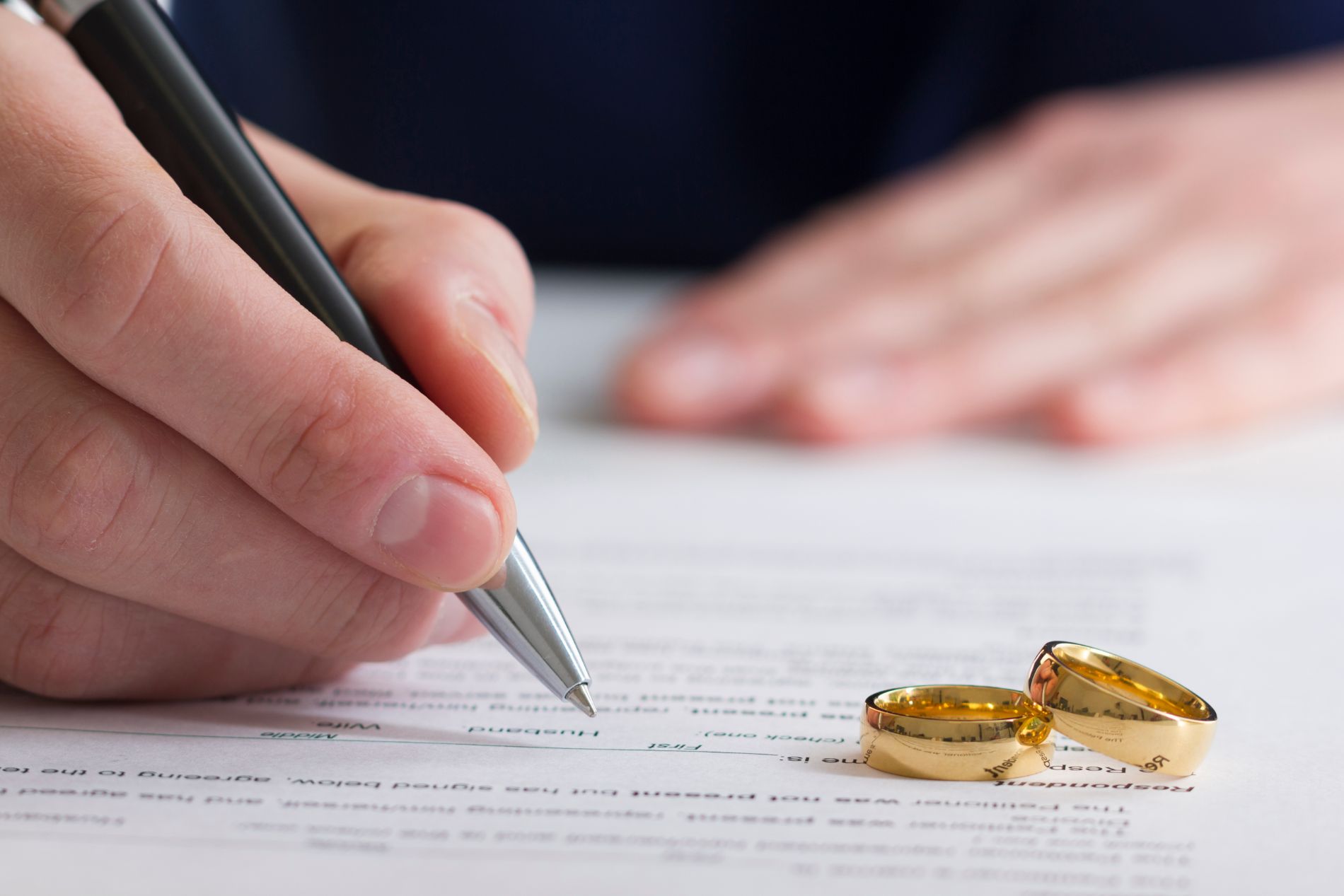 Una persona che firma i documenti del divorzio con le fedi nuziali nelle vicinanze.