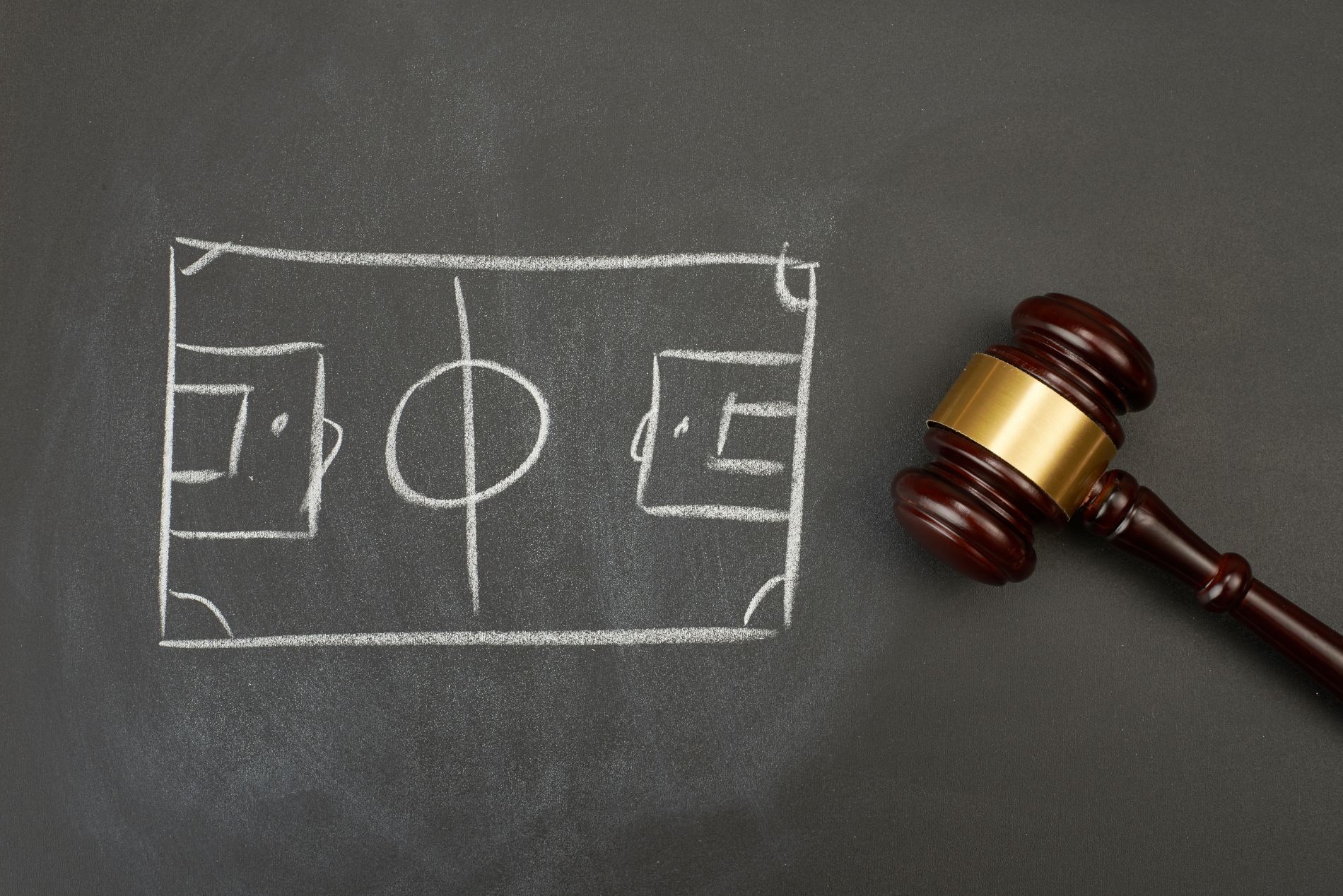 Disegno di un campo da calcio accanto al martelletto di un giudice su una superficie scura.