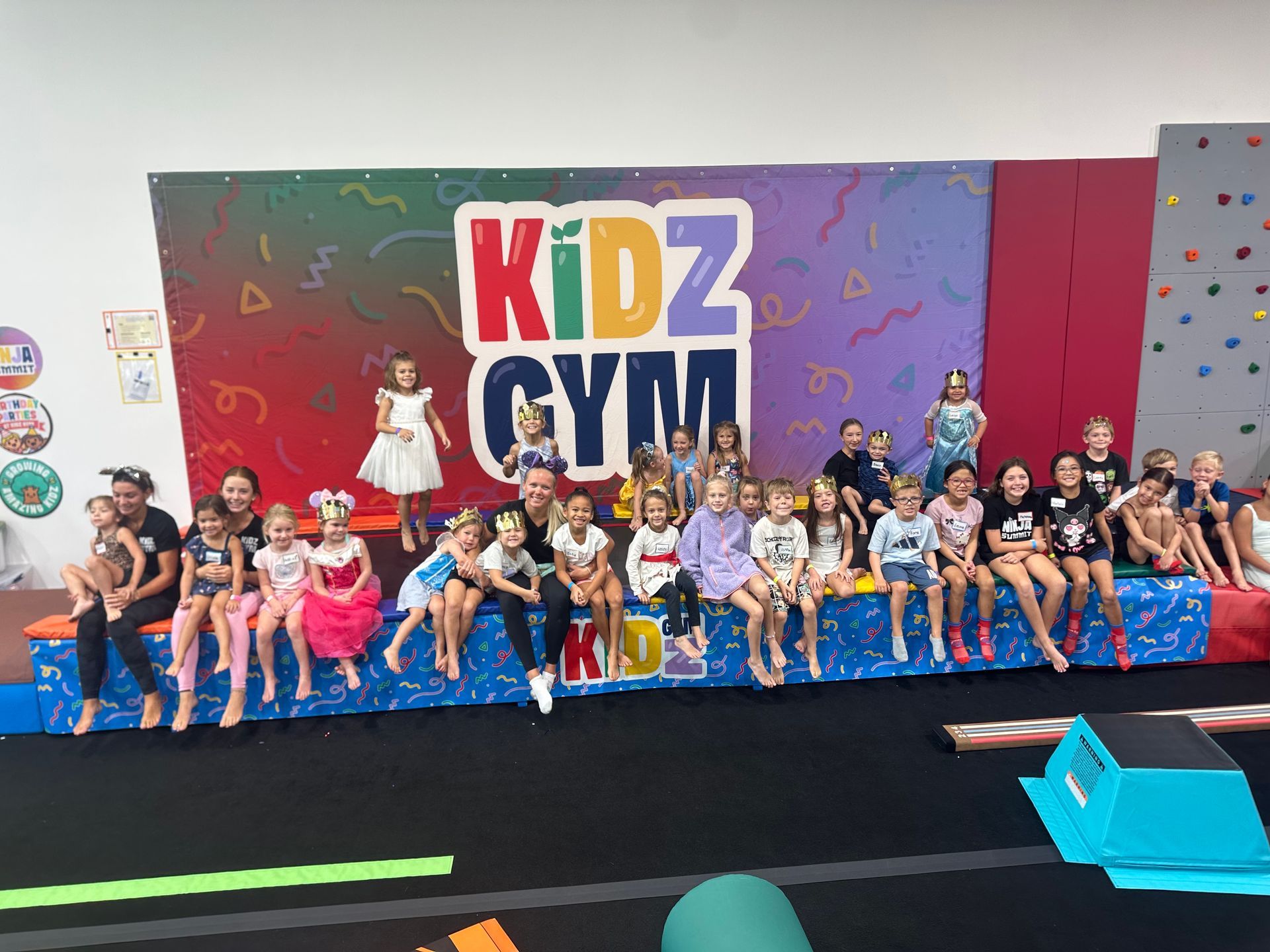 Children playing on colorful gym equipment in a cheerful room with tree decorations.