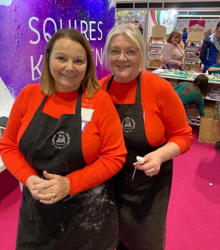 Two women wearing aprons are posing for a picture at a convention.