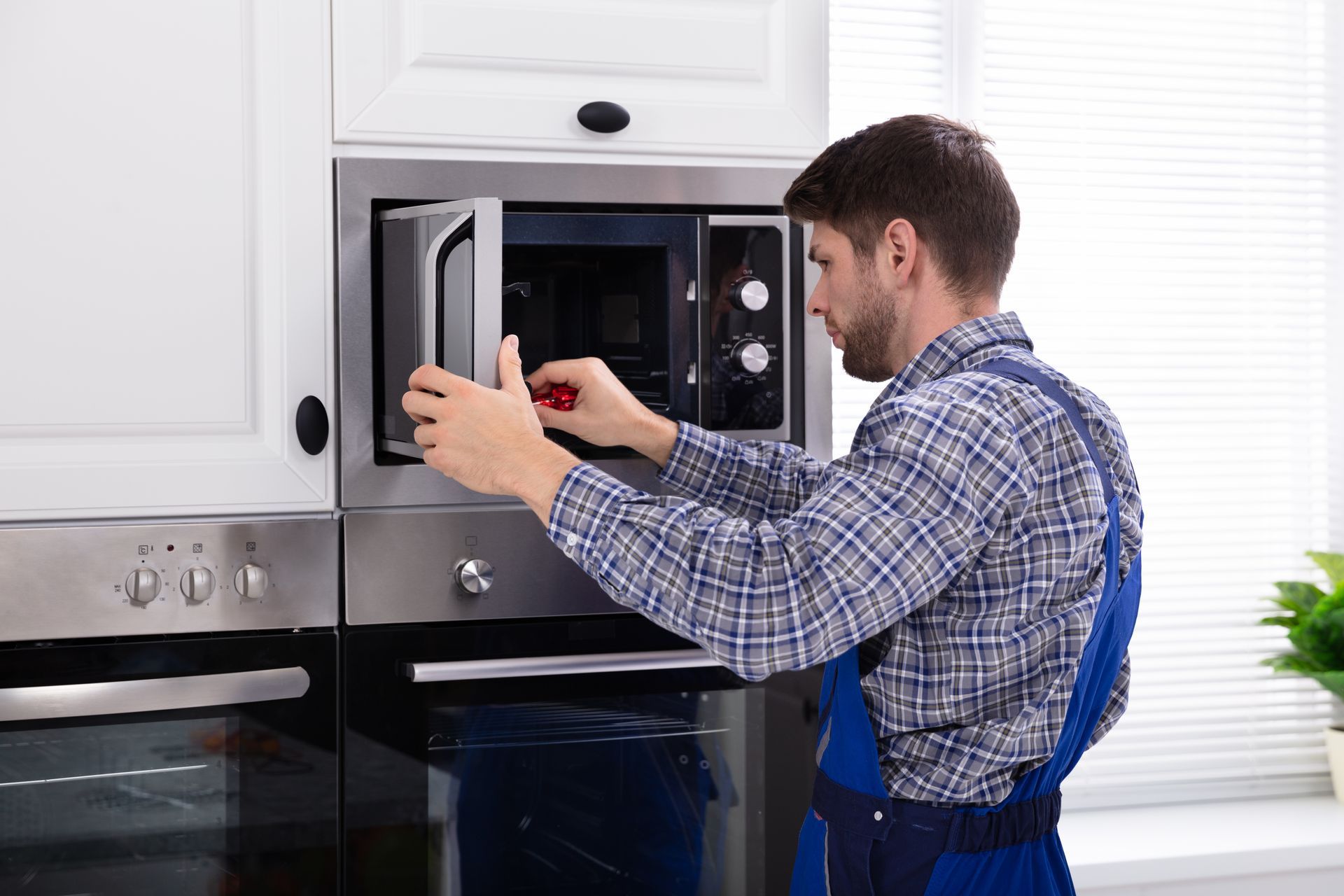 Man in blue apron repairing a microwave in a bright kitchen