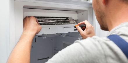 Technician repairing an open wall-mounted air conditioner with a screwdriver