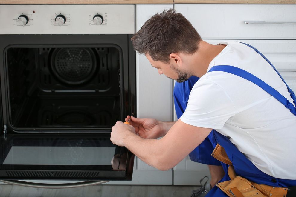 Person in blue overalls repairing a built-in oven in a kitchen
