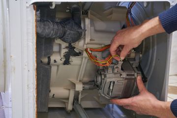 Hands removing a car interior component with wires exposed inside a white vehicle.