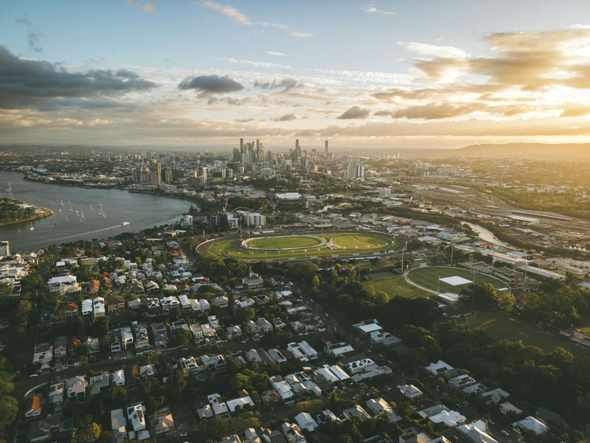 Aerial view of a city skyline at sunset with a river, parks, and residential neighborhoods below
