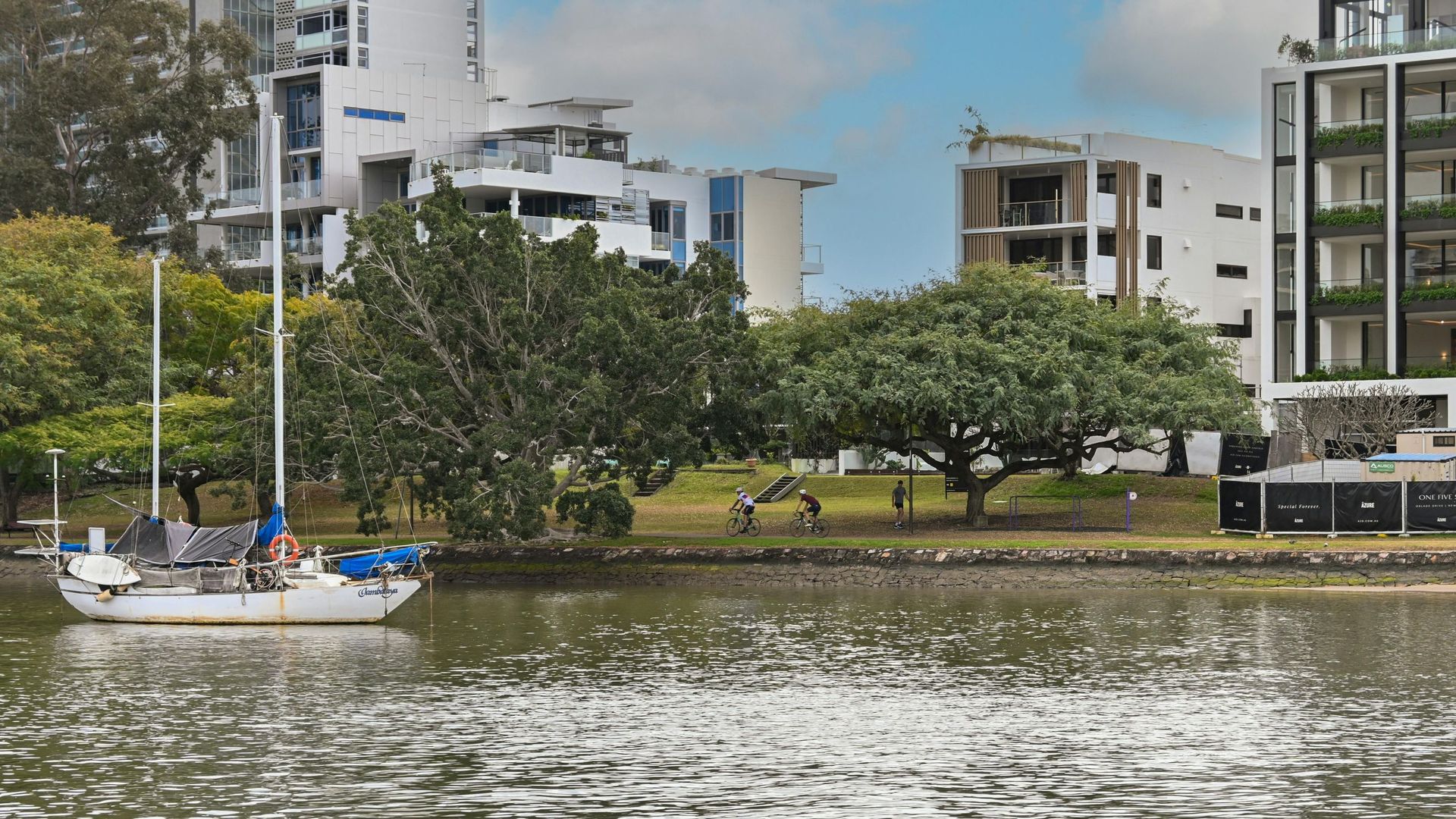 Riverfront cityscape with boats, trees, and modern buildings reflected in the water