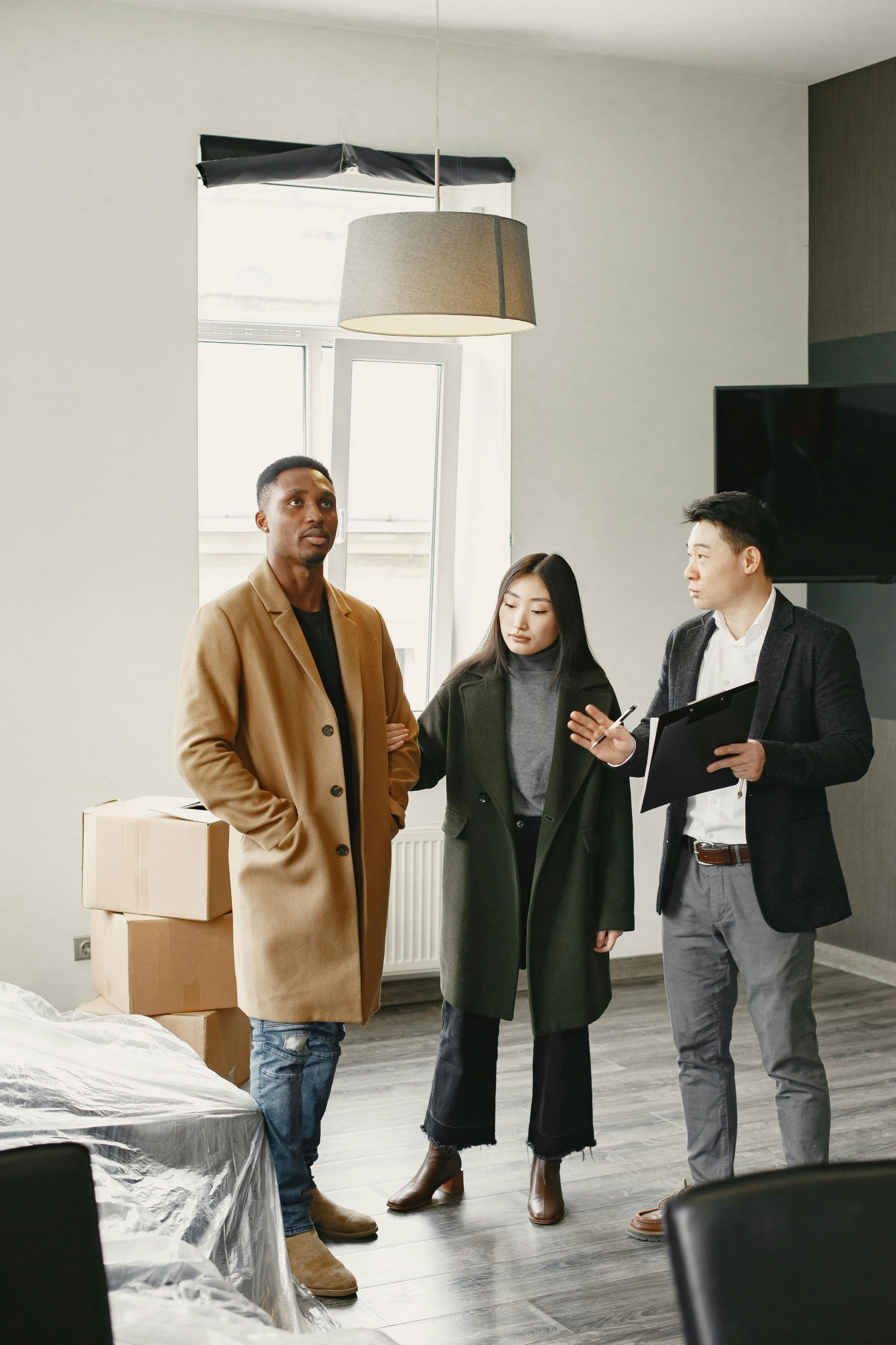 Three people discussing in a bright, modern living room with furniture covered in plastic.