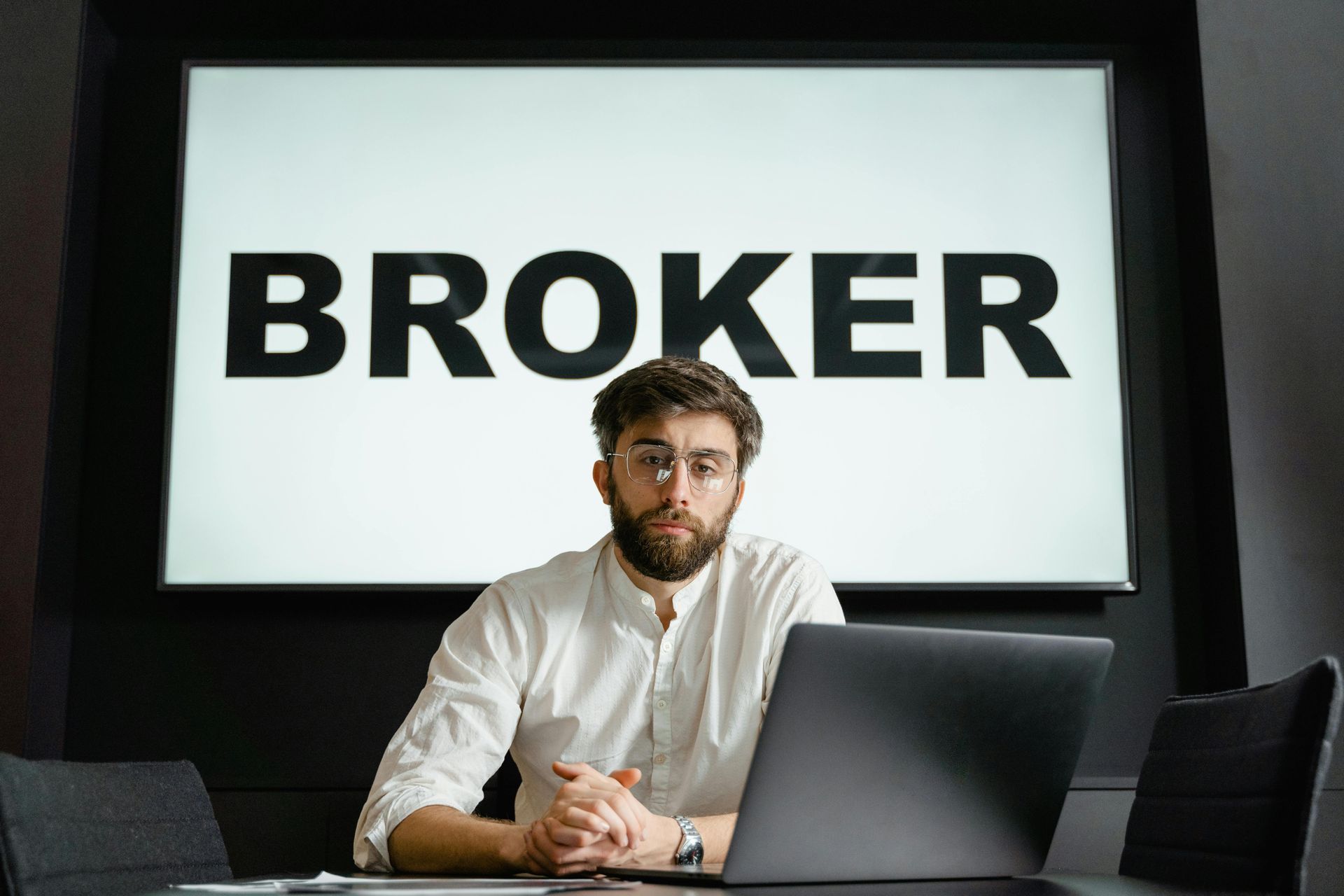 Broker seated at a desk before a screen reading “BROKER”