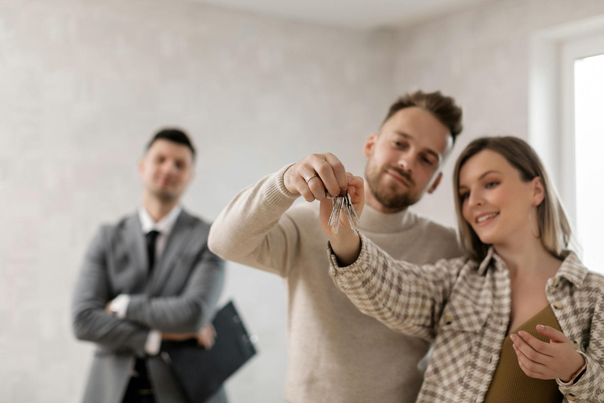Agent and clients smiling while viewing keys in a bright room, with a man blurred in the background