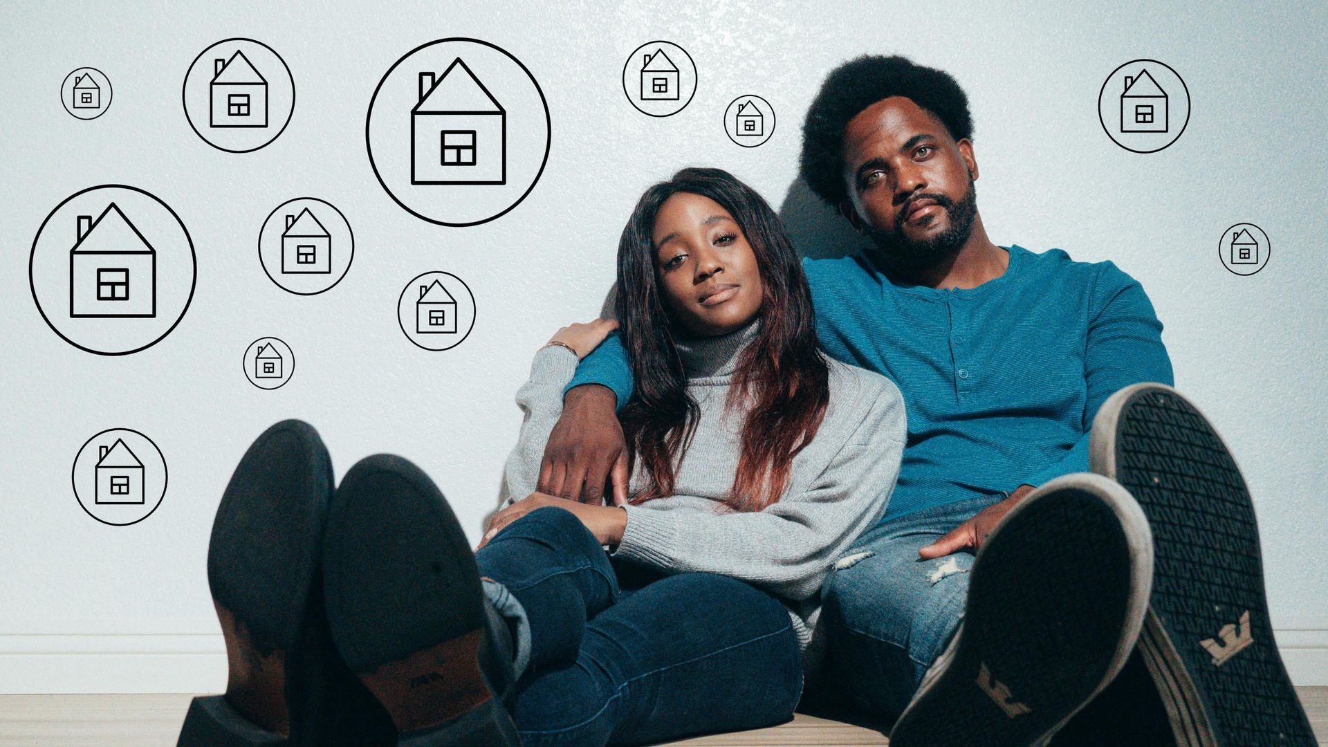 Couple sitting on the floor in a room with house icons on the wall, looking relaxed and smiling.