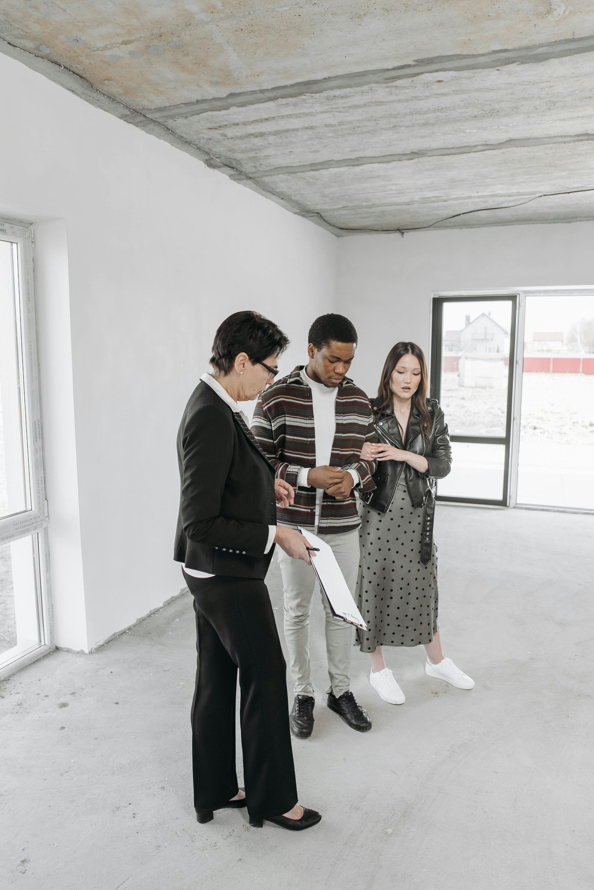 Three people examining a phone in an unfinished room with concrete ceiling and large windows.