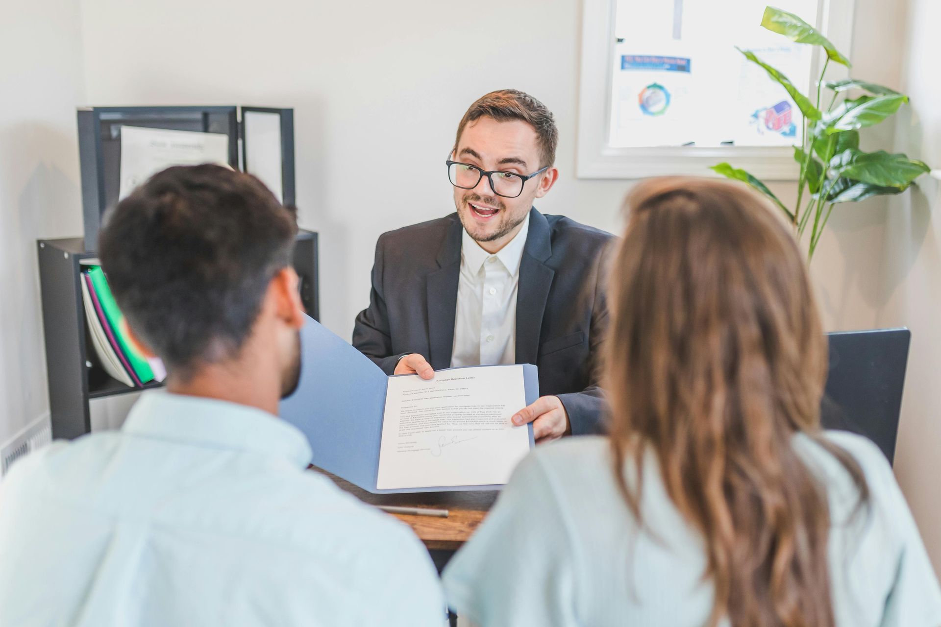 Business meeting with three people discussing documents across a desk in a bright office