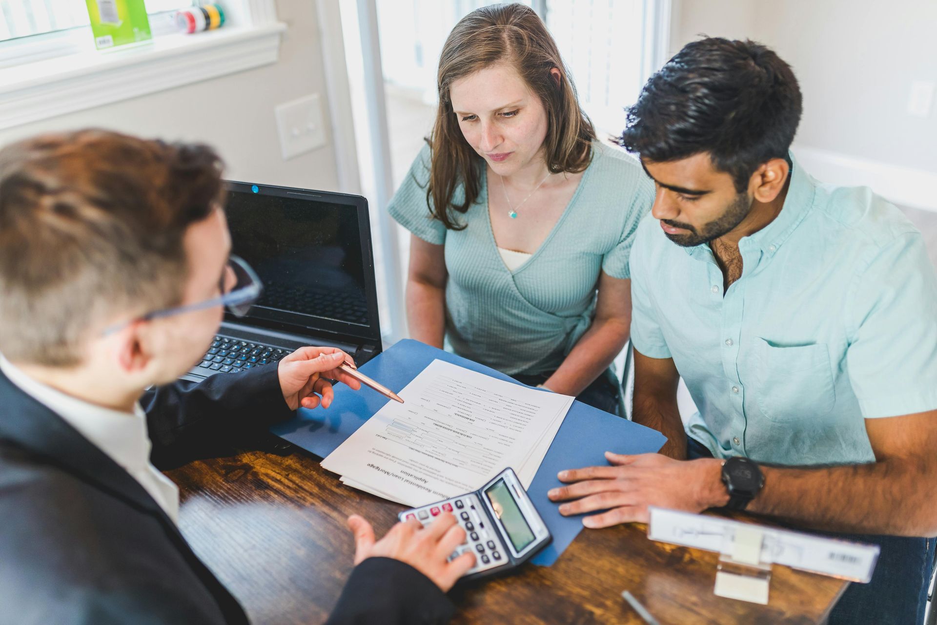 Three people review documents and a laptop at a desk in a bright office.