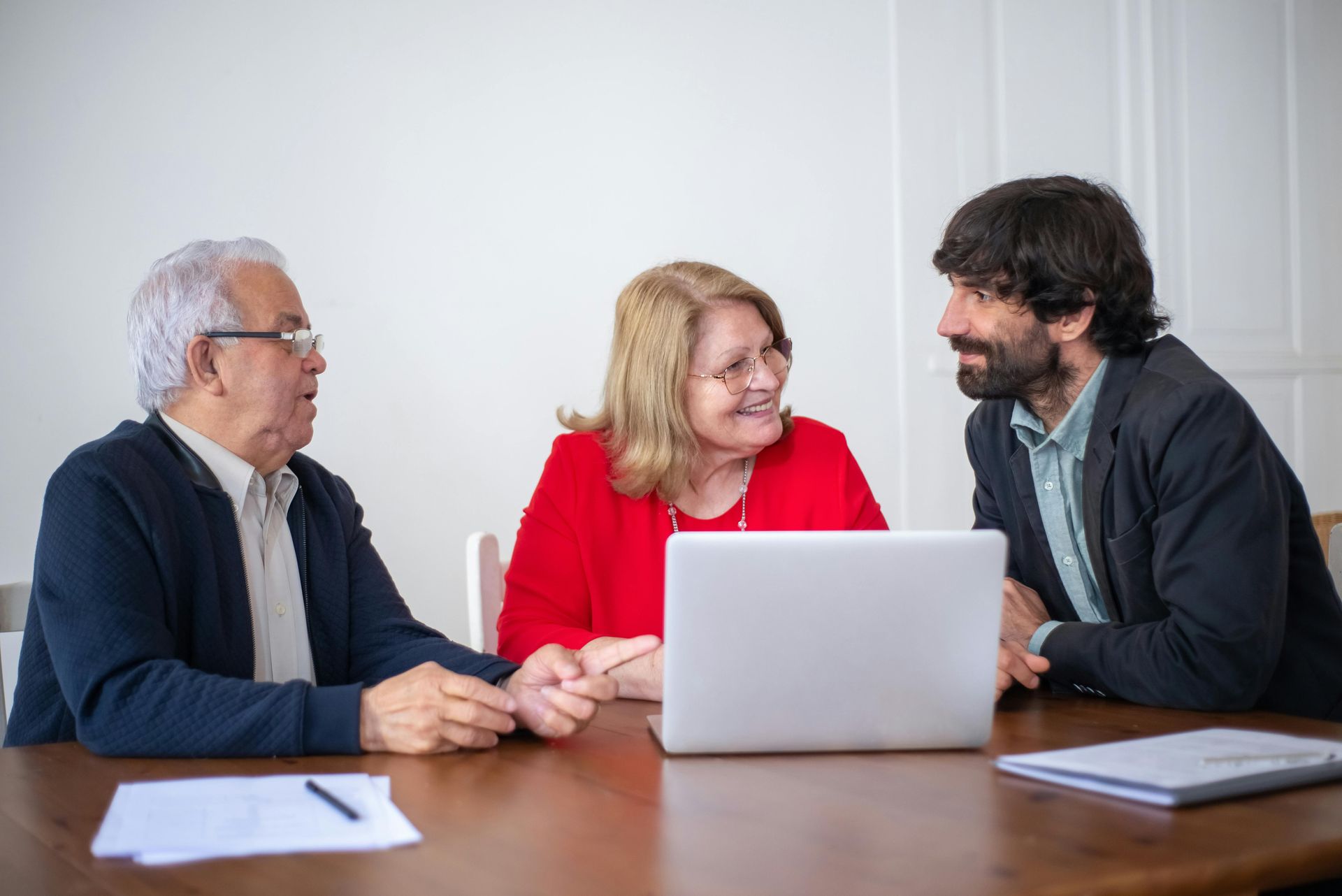 Three people in a meeting around a laptop, smiling and talking at a table.