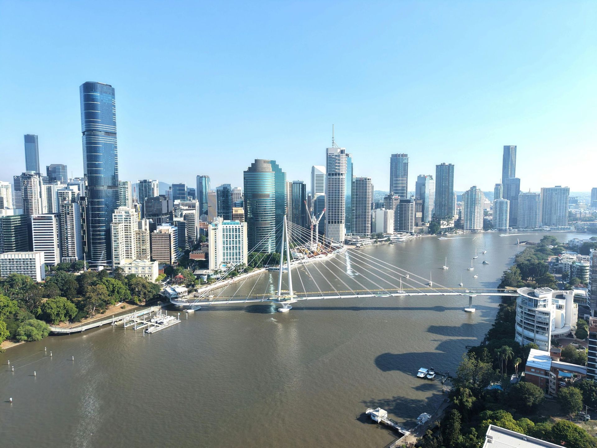 City skyline over a wide river with a cable-stayed bridge under a clear blue sky.