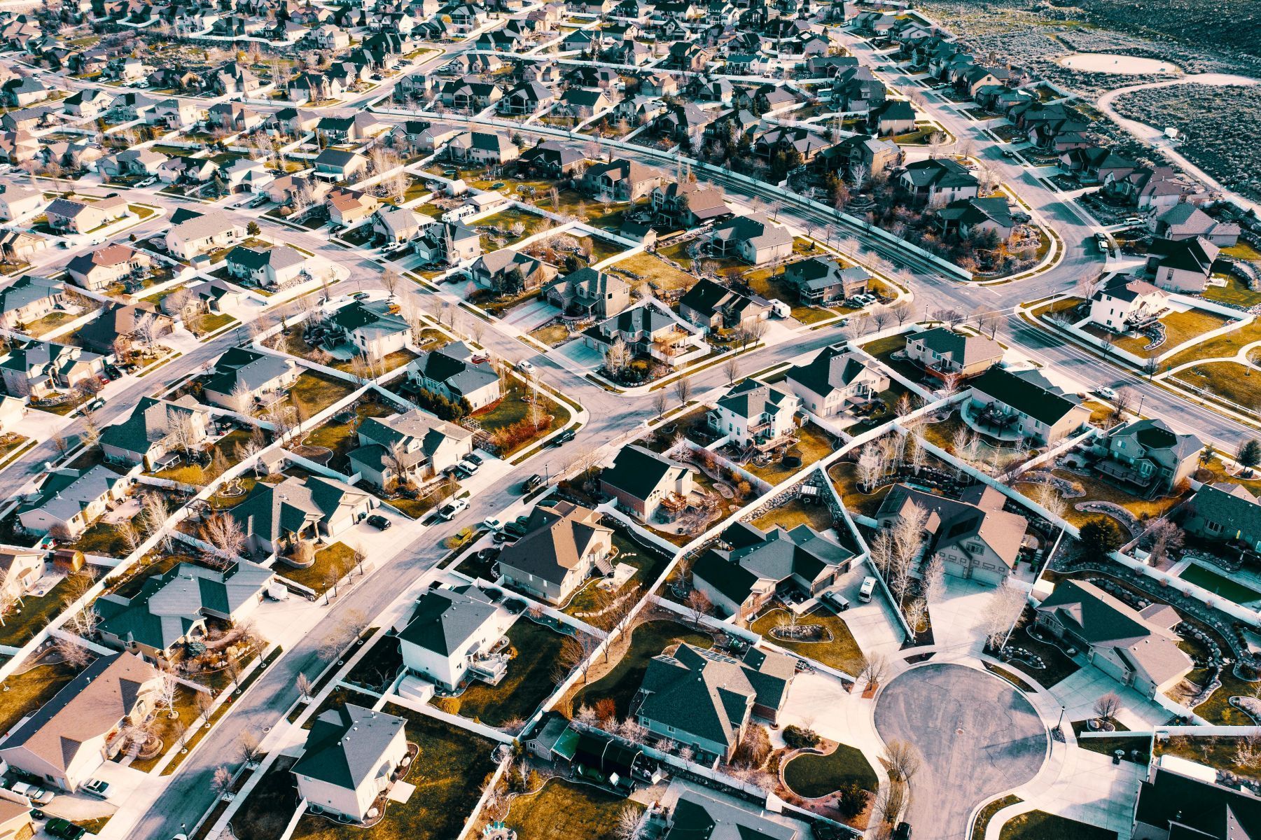Aerial view of a suburban neighborhood with houses, streets, and a central cul-de-sac under bright daylight