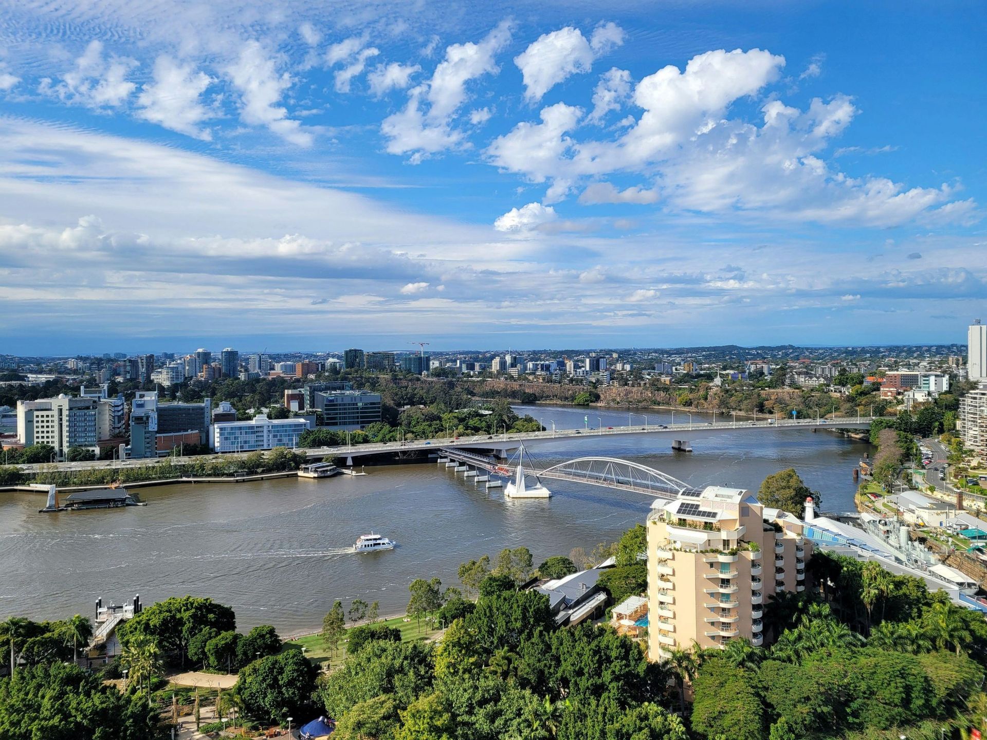 Wide river cityscape with a bridge, boats, and buildings under a bright blue sky