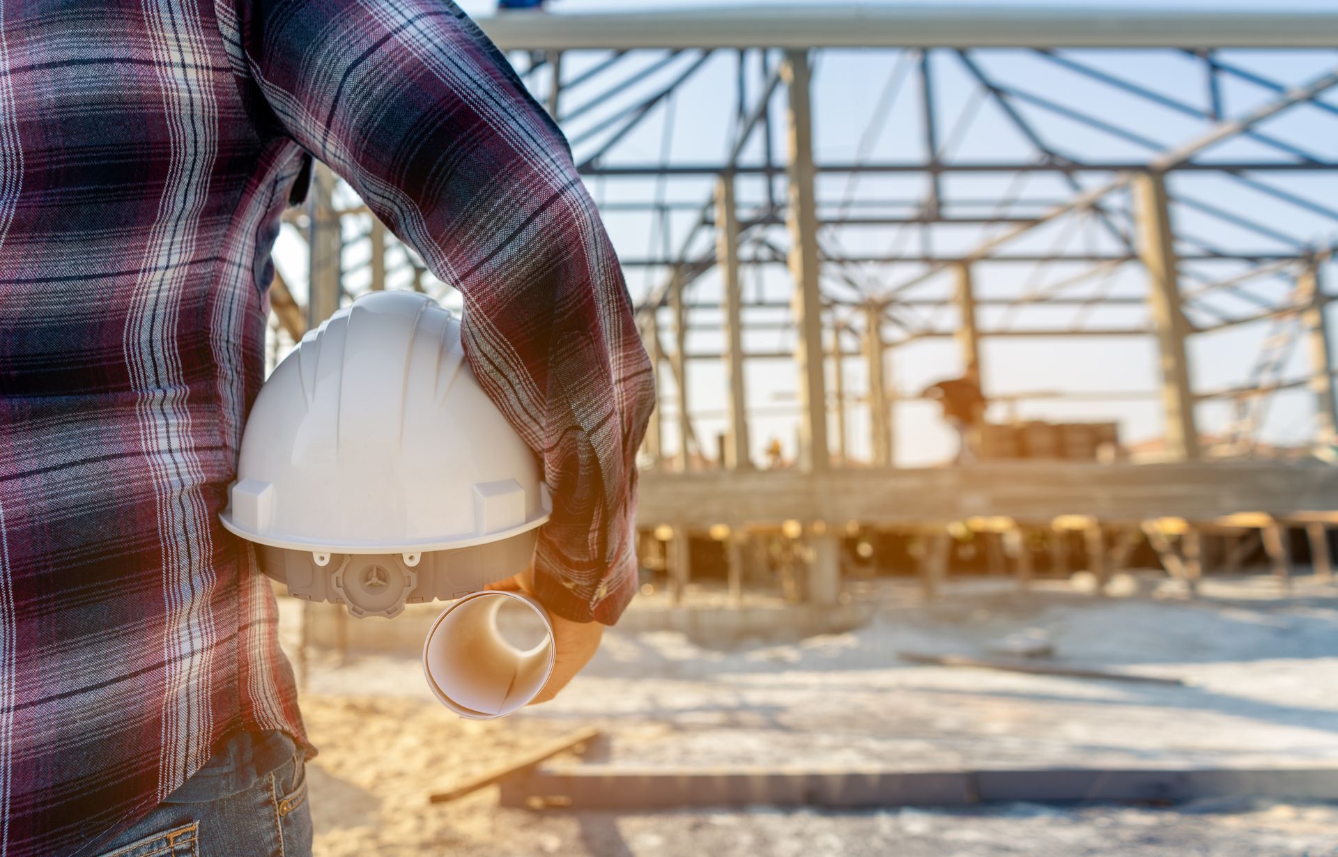 Construction worker holding a hard hat, standing in front of a building frame. Construction worker holding a hard hat, standing in front of a building frame.