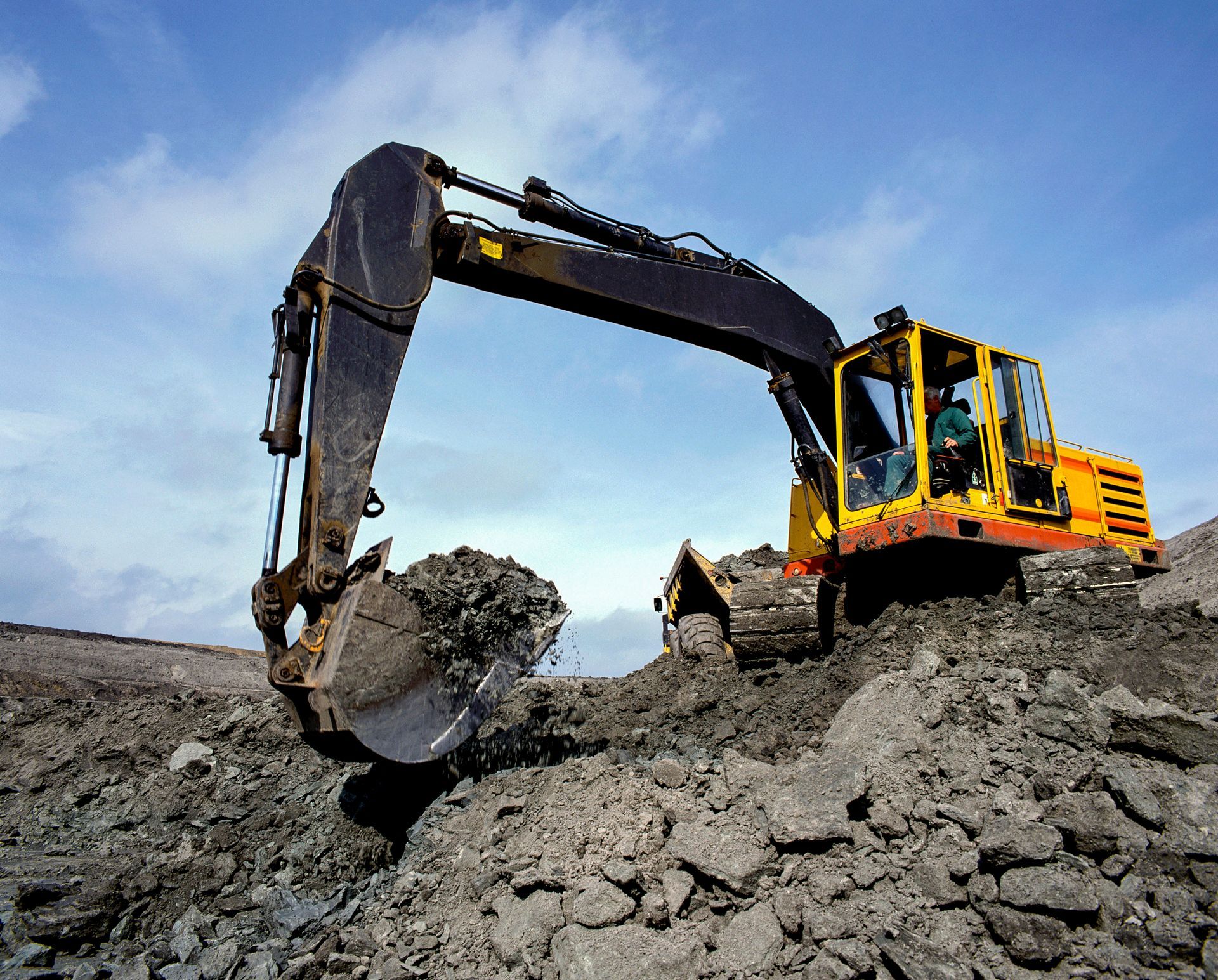 Yellow excavator digging into dark earth under a cloudy sky. Yellow excavator digging into dark earth under a cloudy sky.
