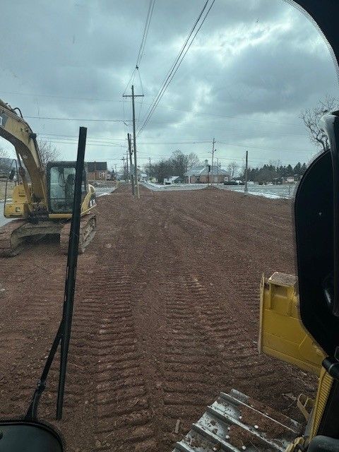 Yellow loader in a quarry, moving material from a large pile of light-colored aggregate. View from a machine cab of a construction site. Dirt road with excavator. Cloudy sky.