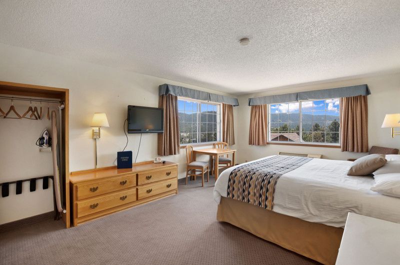 A hotel room with a king size bed and a flat screen, closet, mini fridge, coffee maker, two windows