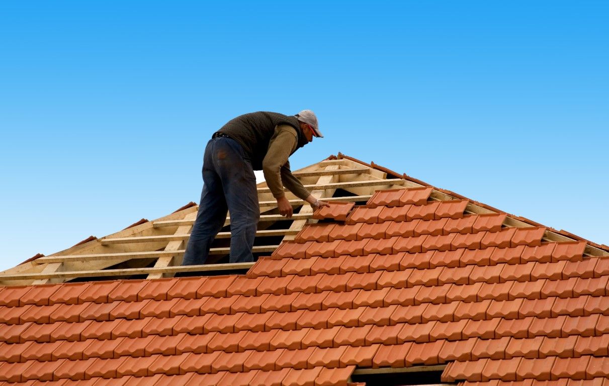 Man installing clay roof tiles on a house under a blue sky.