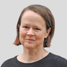 Porträtfoto von Sabine Benzer, Jurorin, mit halblangem braunem Haar und dunklem Oberteil vor neutralem Hintergrund.