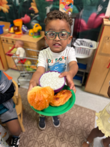Child holding a green plate with assorted pastries at a bakery counter