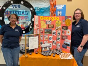 Two women stand beside a Georgia display board at a table with books and pamphlets.