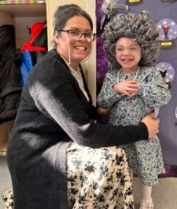 Woman posing with a child in a festive outfit, both smiling indoors by a purple backdrop.
