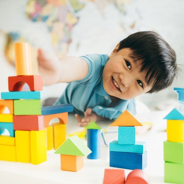 Child smiling and reaching over colorful stacking blocks on a table
