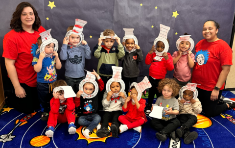 Group of children and two adults in costumes posing in a classroom with a starry backdrop