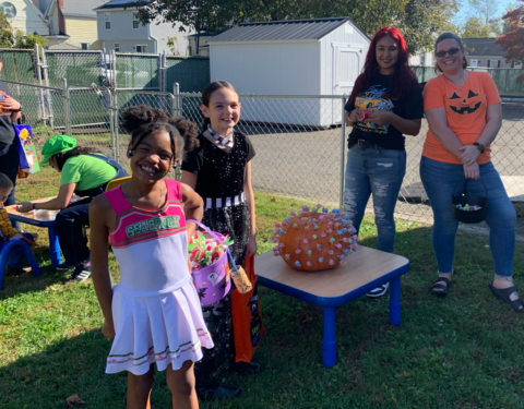 Children and adults at a backyard party, with kids posing by a table holding a spiky orange ball.