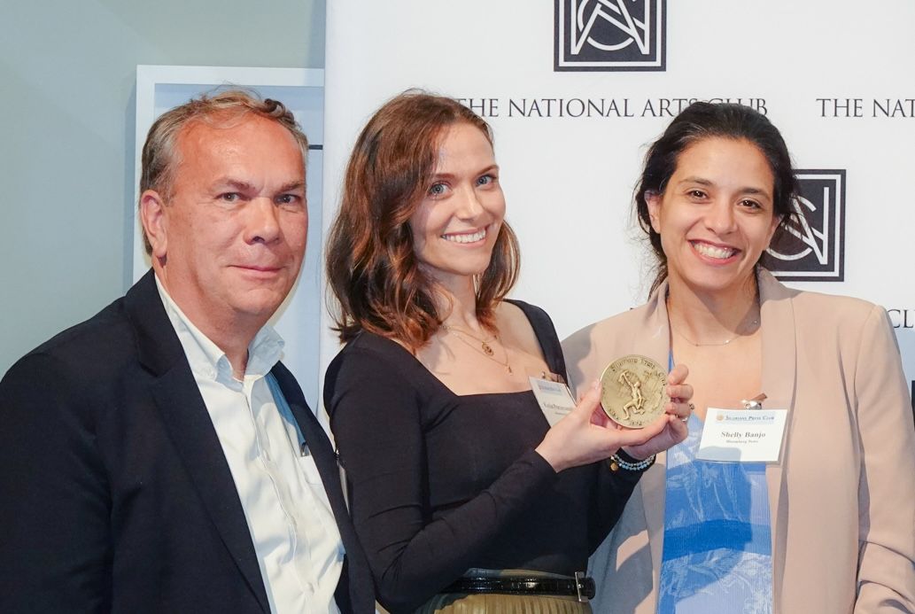 Three people pose with a golden medal in front of a white backdrop.