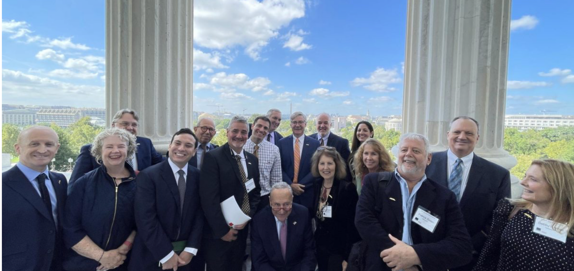 Group of people pose outside with columns and a city view.