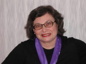 Woman with short dark hair, glasses, and a purple scarf smiles.