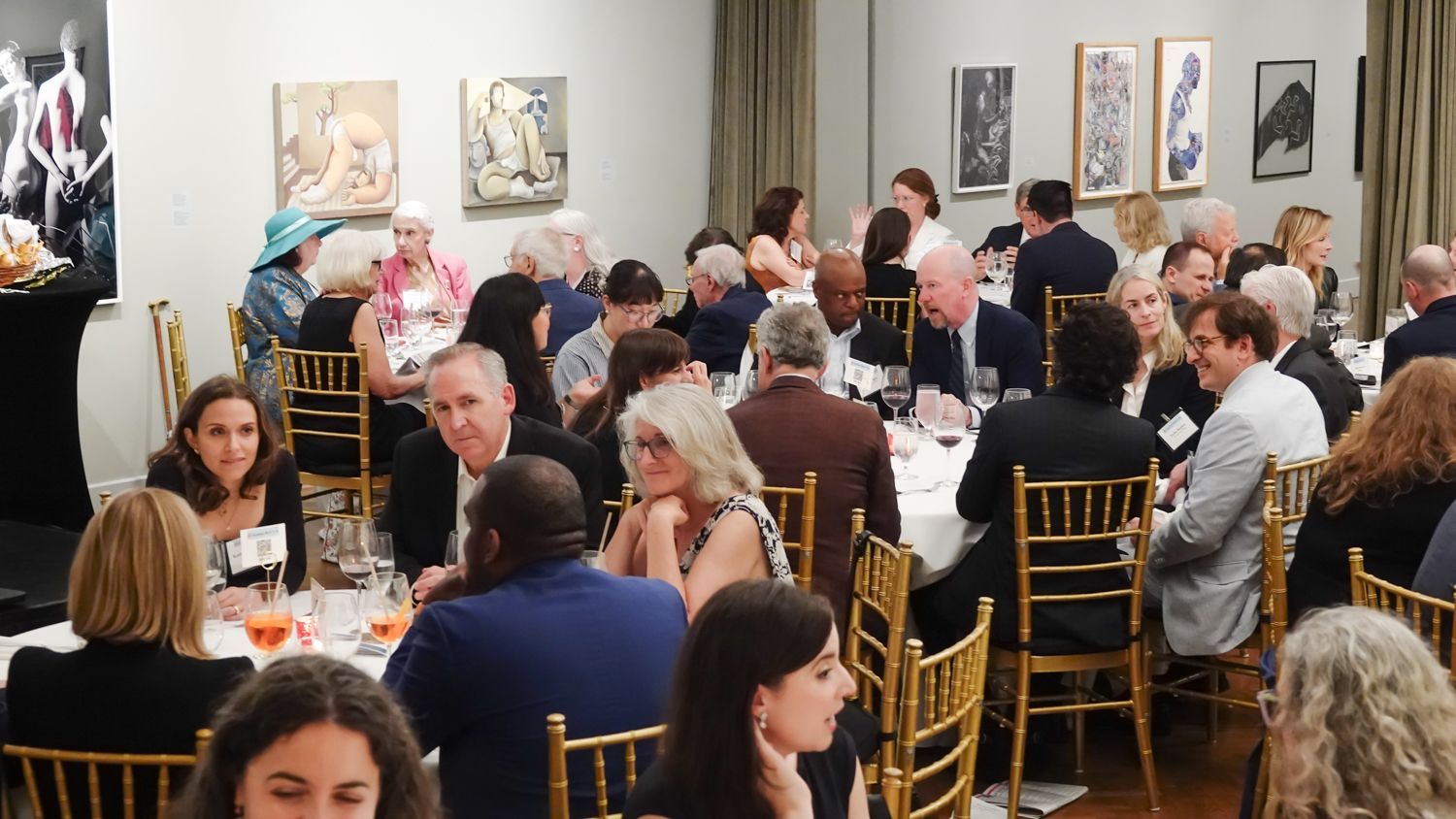 People seated at tables in a room with artwork on the walls, attending an event.